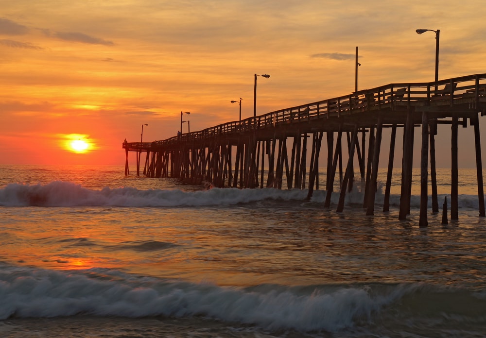 The rising sun peeks through clouds and is reflected in waves by the Nags Head fishing pier on the outer banks of North Carolina
